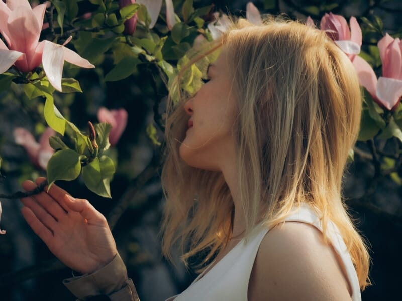 Femme blonde de profil touchant délicatement une fleur rose dans un jardin lors d'un shooting photo lifestyle à Maisons-Laffitte