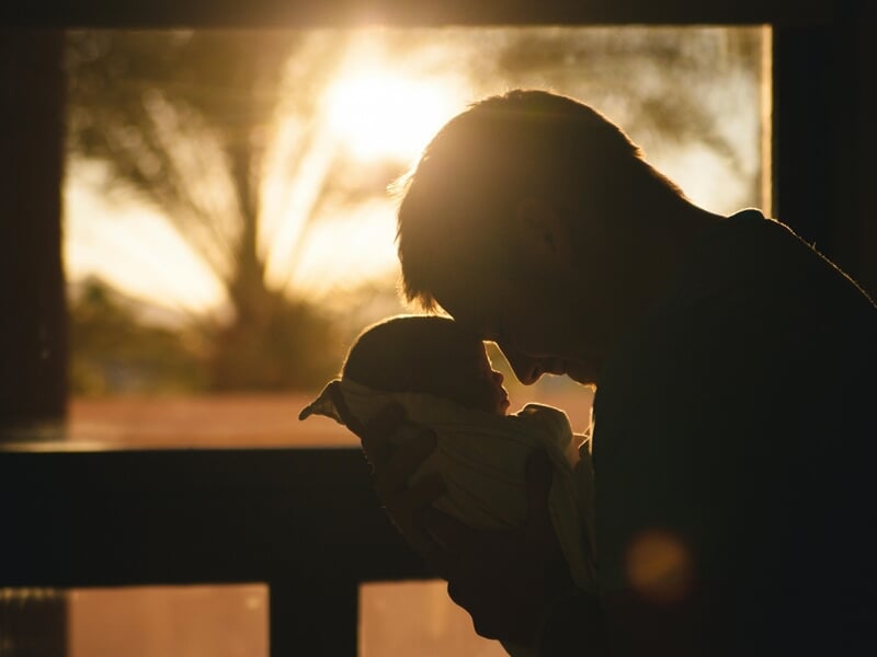 Silhouette d'un père tenant tendrement son bébé devant une fenêtre lors d'un shooting avec un photographe bébé à Maisons-Laffitte.