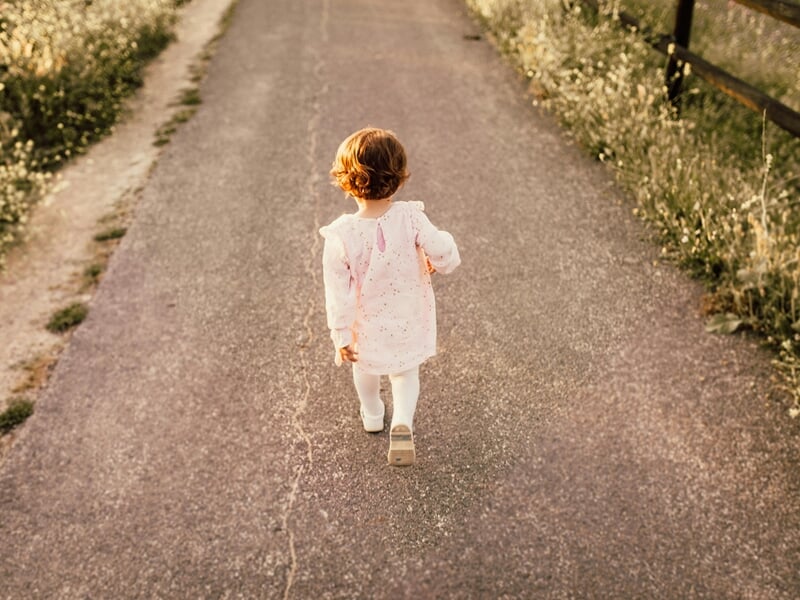 Une petite fille marche seule sur un chemin entouré de végétation, lors d'un shooting avec un photographe bébé à Maisons-Laffitte.