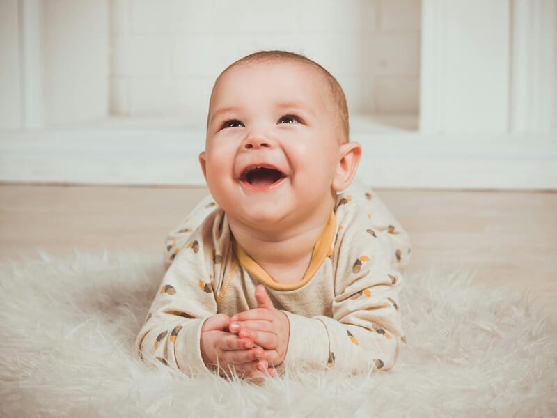 Bébé souriant allongé sur un tapis moelleux blanc, lors d'un shooting avec un photographe bébé à Maisons-Laffitte.