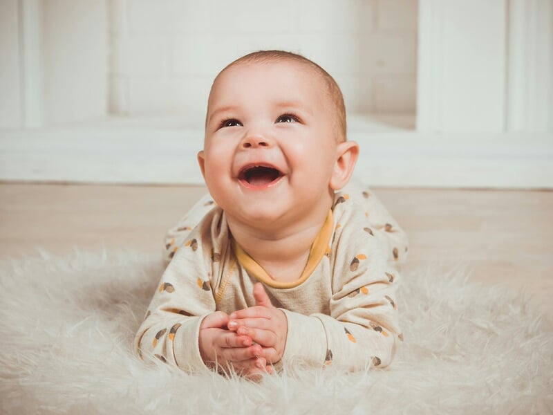 Bébé souriant allongé sur un tapis moelleux blanc, lors d'un shooting avec un photographe bébé à Maisons-Laffitte.