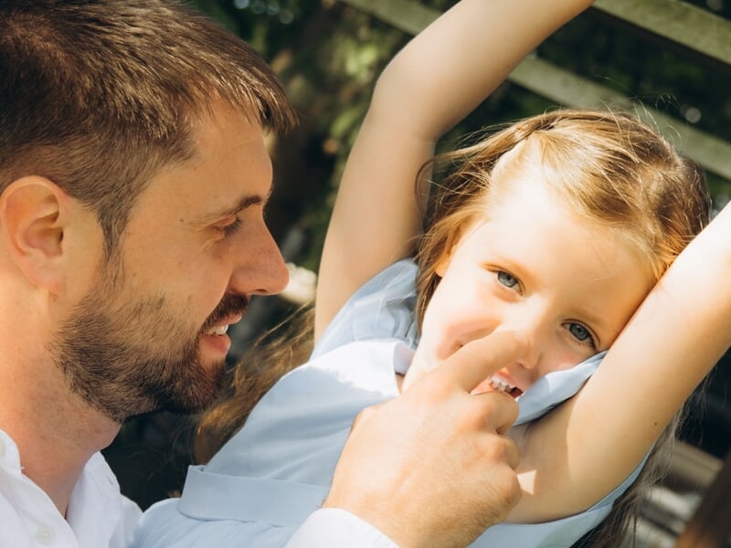 Un homme souriant joue avec une petite fille aux cheveux blonds lors d'un shooting photo famille à Maisons-Laffitte.