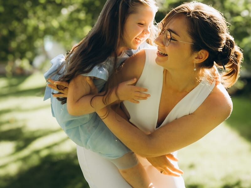 Une femme joyeuse porte une petite fille en robe bleue lors d'un shooting photo famille à Maisons-Laffitte.