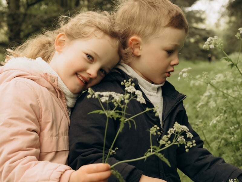 Deux enfants, une fille et un garçon, tiennent des fleurs sauvages lors d'un shooting photo famille à Maisons-Laffitte.