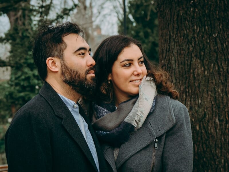 Un couple pose ensemble dans un parc, l'homme regarde au loin tandis que la femme sourit lors d'un shooting photo couple à Maisons-Laffitte.