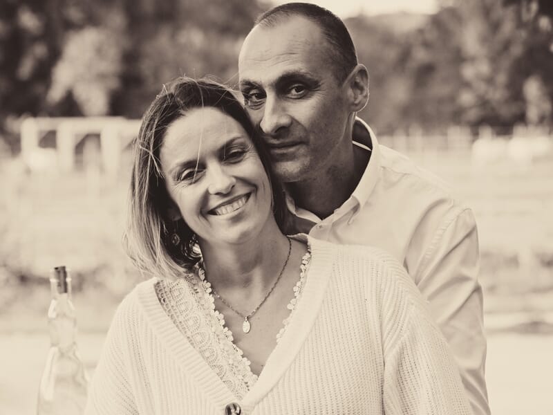 Couple souriant en extérieur, ambiance douce et chaleureuse, photo en noir et blanc avec arrière-plan flou.