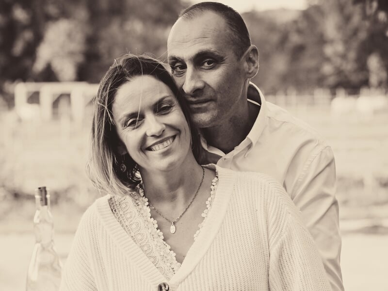 Couple souriant en extérieur, ambiance douce et chaleureuse, photo en noir et blanc avec arrière-plan flou.