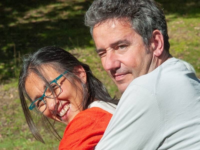 Un couple souriant en extérieur, à l'occasion d'un shooting photo à Biarritz. La femme porte des lunettes et un pull orange, l'homme est en blanc.