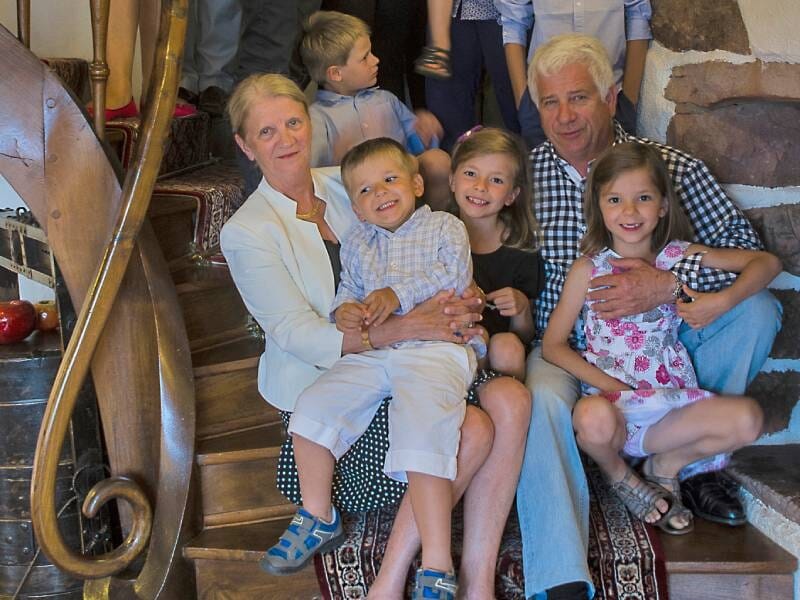 Une famille souriante assise sur un escalier en bois avec un tapis, entourée d'enfants et d'adultes dans une maison chaleureuse.