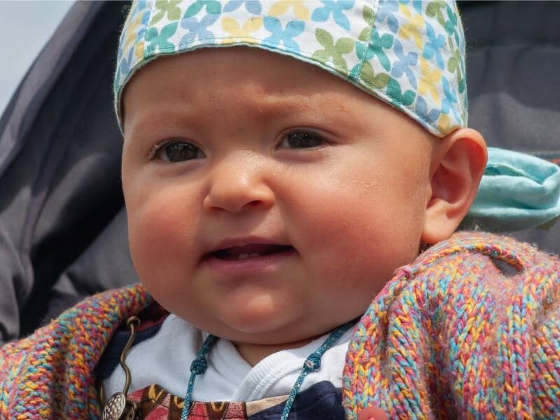 Portrait d'un bébé avec un bonnet coloré et un pull en laine, regardant vers l'avant avec une expression douce.