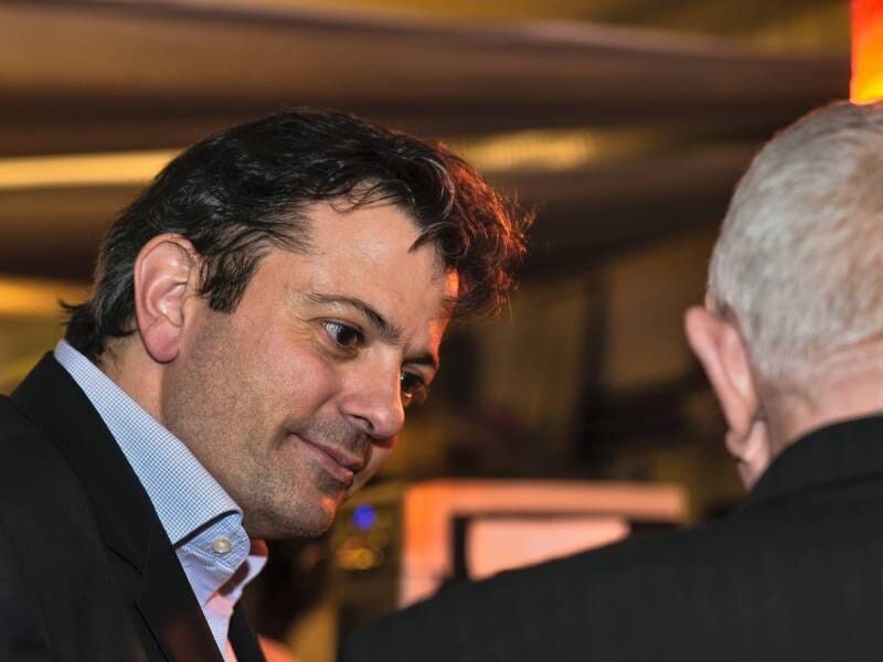 Homme en costume souriant, discutant avec une autre personne dans un cadre intérieur chaleureux et tamisé.