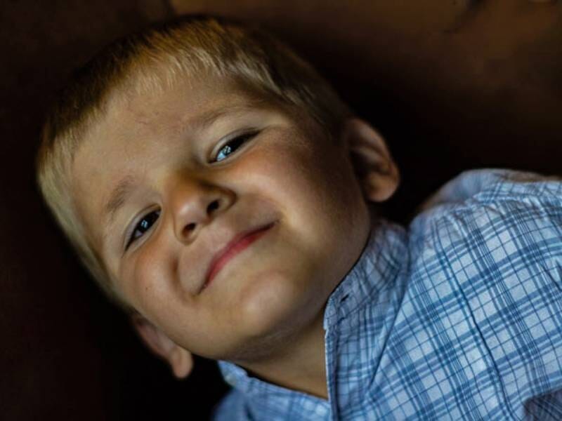 Portrait d'un jeune garçon souriant, portant une chemise à carreaux bleue, dans un environnement sombre, lors d'un shooting photo portrait à Biarritz.