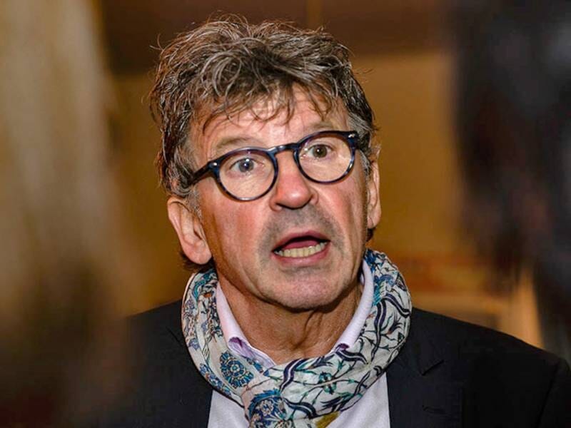 Homme âgé avec lunettes et écharpe colorée, exprimant une émotion forte dans un lieu intérieur.