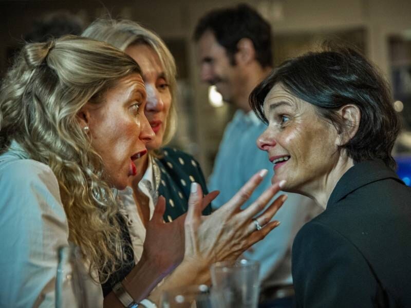Quatre personnes échangent avec animation dans un lieu chaleureux, deux femmes au premier plan en pleine conversation.