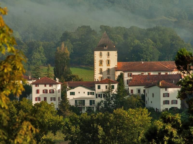 Vue du village de Sare avec ses maisons blanches et toits rouges, entouré d'arbres verts sous un ciel brumeux, lors d'un stage photo.