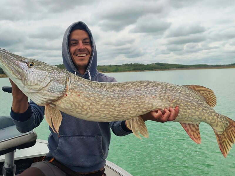 Jeune homme en sweat à capuche tenant un grand brochet sur un bateau lors d'un stage de pêche à Toulouse.