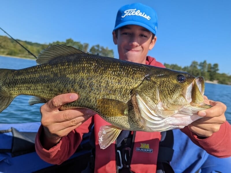 Un adolescent en casquette bleue exhibe un gros poisson noir et jaune lors d'un stage de pêche dans l'Ain.