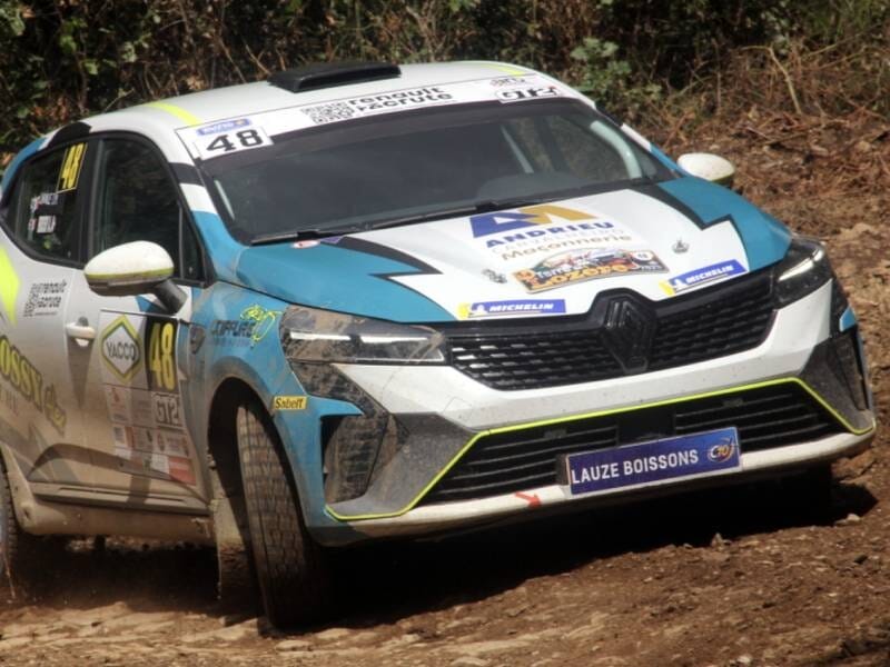 Voiture de rallye Renault blanche et bleue sur circuit terre d'Issoire, en pleine course sur terrain boueux.