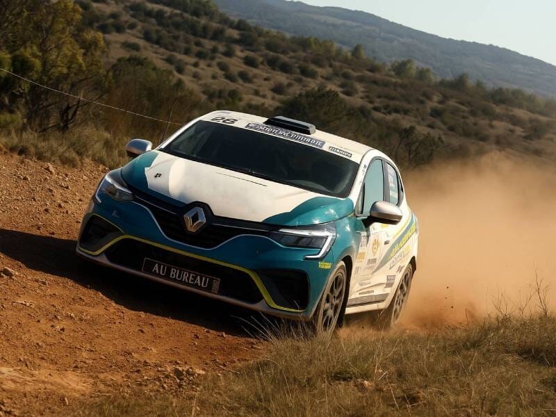 Voiture de rallye Renault blanche et bleue sur le circuit terre d'Issoire, dérapant dans un virage avec poussière soulevée lors d'un stage de pilotage.