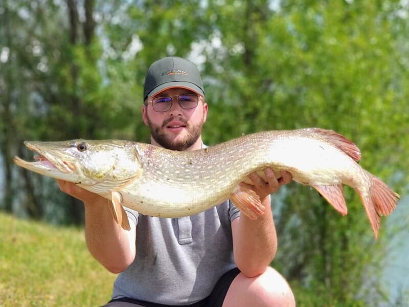Jeune homme avec casquette et lunettes tenant un grand brochet lors d'un stage de pêche près de Dijon.