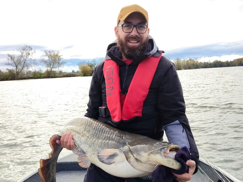 Homme barbu avec lunettes et gilet de sauvetage tenant un gros poisson lors d'un stage de pêche près de Dijon.
