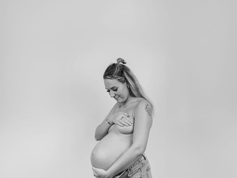 Femme enceinte en noir et blanc, posant de profil avec un sourire doux lors d'un shooting photo grossesse à Dunkerque.