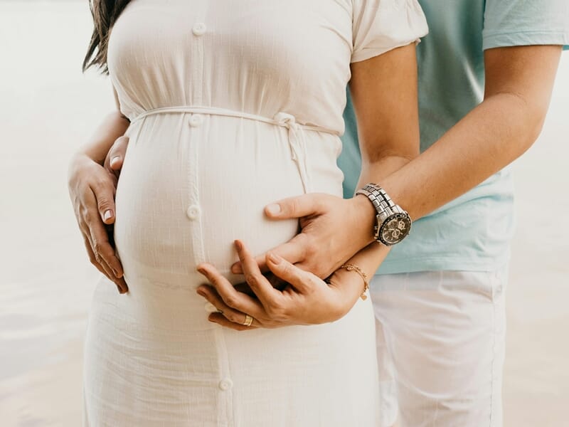 Couple au bord de l'eau, homme et femme enceinte en robe blanche lors d'un shooting photo grossesse à Dunkerque.