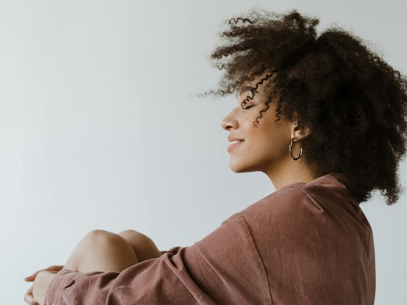 Femme aux cheveux bouclés assise de profil, portant une chemise marron lors d'un shooting photo portrait à Dunkerque.