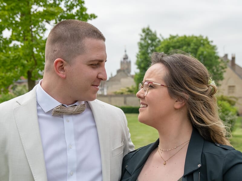 Un couple souriant se regarde tendrement dans un parc avec des arbres lors d'un shooting photo couple à Dunkerque.