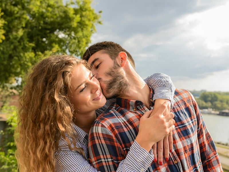 Un couple s'embrasse tendrement au bord d'une rivière lors d'un shooting photo couple à Dunkerque.