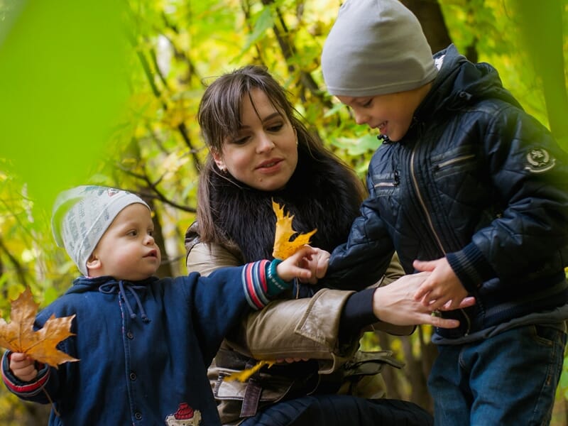 Une femme avec deux enfants jouant avec des feuilles d'automnelors d'un shooting photo famille à Dunkerque.