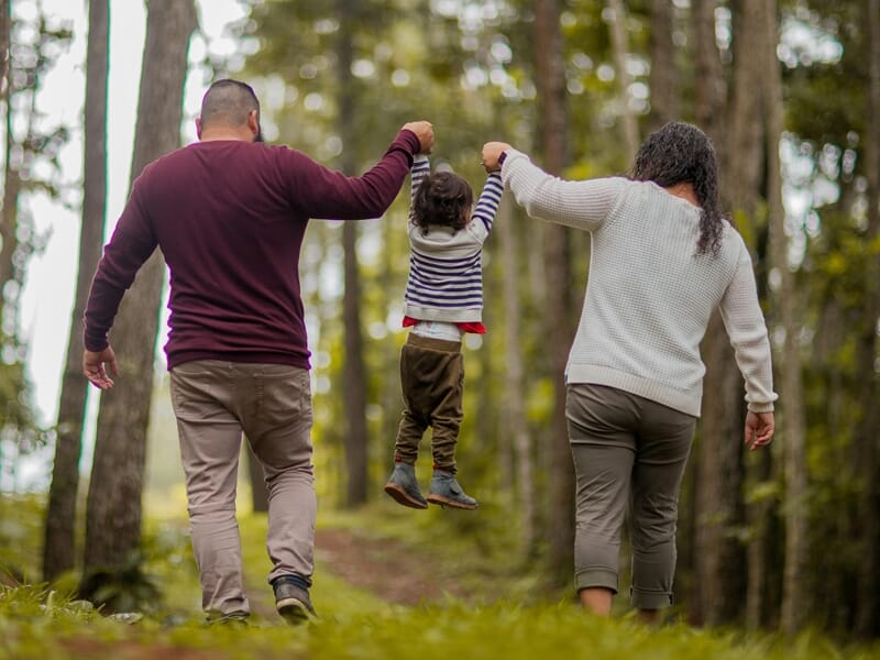 Parents tenant les mains de leur enfant qui est suspendu entre eux lors d'un shooting photo famille à Dunkerque.