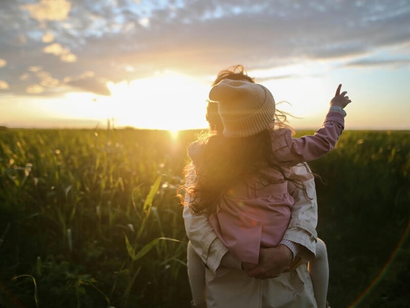 Une personne porte un enfant dans un champ au coucher du soleil, lors d'un shooting photo lifestyle à Dunkerque.