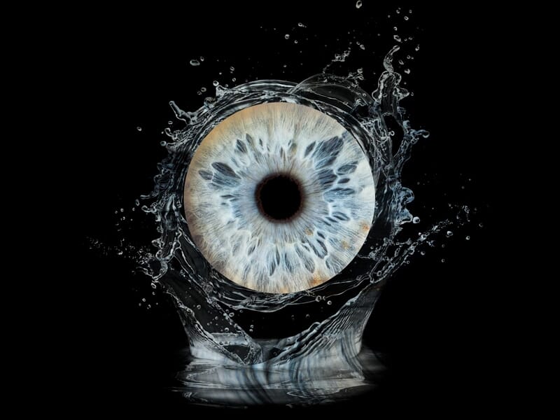 Un iris bleu clair en gros plan avec des éclaboussures d'eau dynamiques sur fond noir, capturant la texture de l'œil.