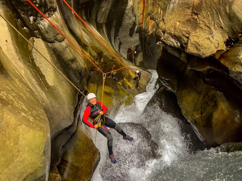 Canyoneur suspendu à une corde dans un canyon étroit avec des parois rocheuses et de l'eau en dessous.