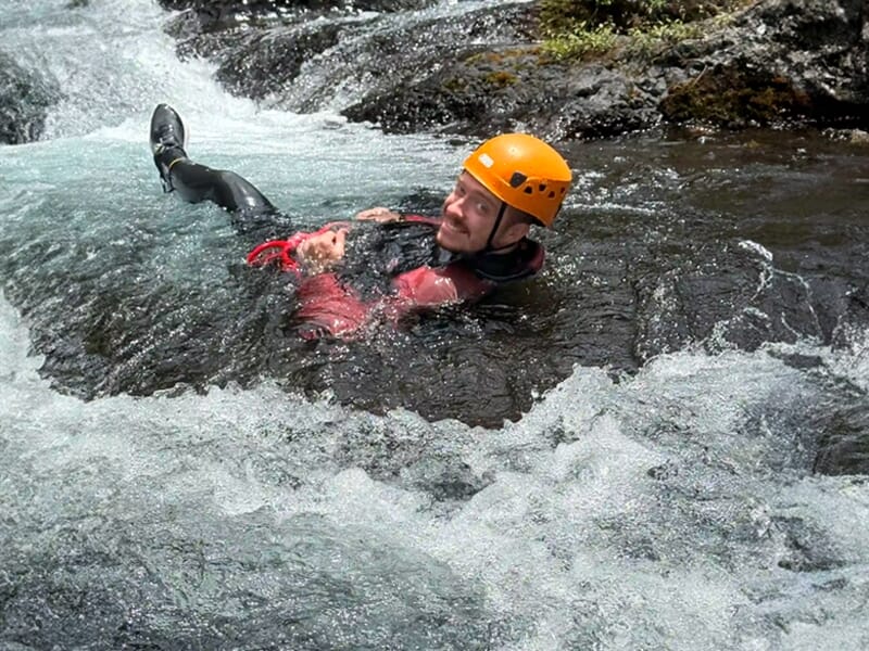Personne en casque orange flottant dans une rivière agitée entourée de rochers et d'eau vive.