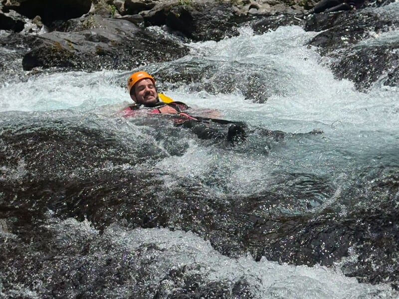Homme en casque orange glissant dans un courant d'eau vive avec des rochers autour, souriant.