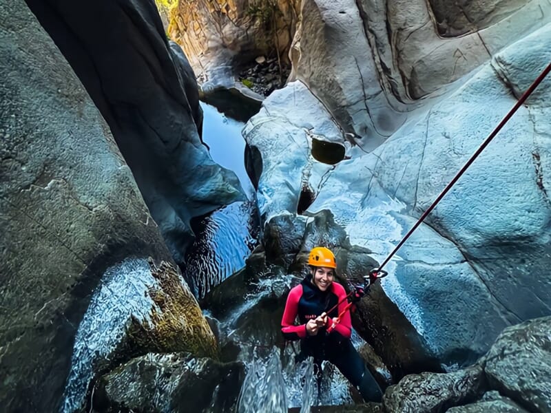 Femme en casque orange descend en rappel dans un canyon étroit aux parois rocheuses blanches et lisses.