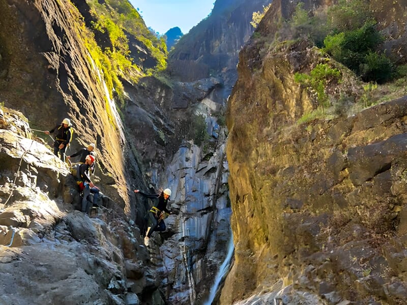 Groupe de personnes en équipement de canyoning dans un canyon rocheux profond sous un ciel bleu ensoleillé.