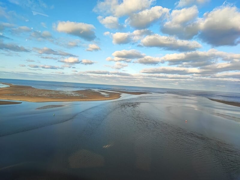 Vue aérienne d'un estuaire avec des bancs de sable et un ciel partiellement nuageux lors d'un baptême en ulm autogire dans le Cotentin.