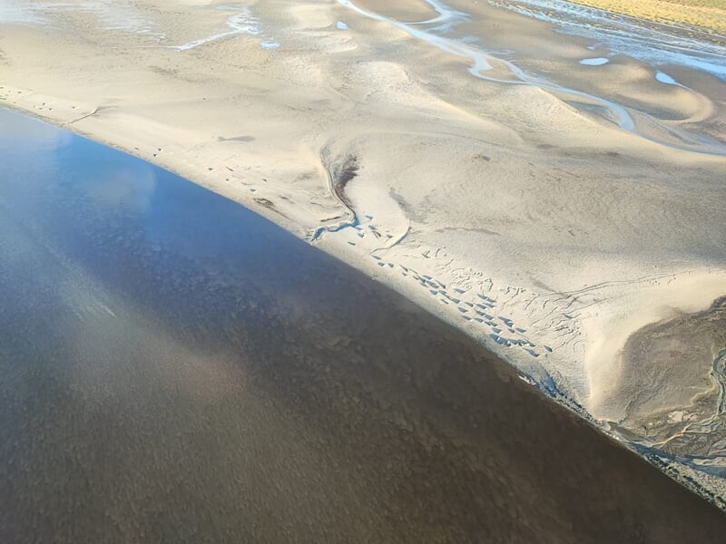 Photo prise du ciel montrant une plage de sable clair et une étendue d'eau sombre lors d'un baptême en ulm autogire dans le Cotentin.