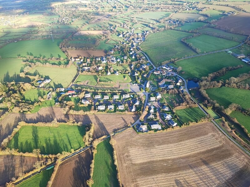 Vue aérienne d'un village entouré de champs verts et bruns lors d'un baptême en ulm autogire dans le Cotentin.