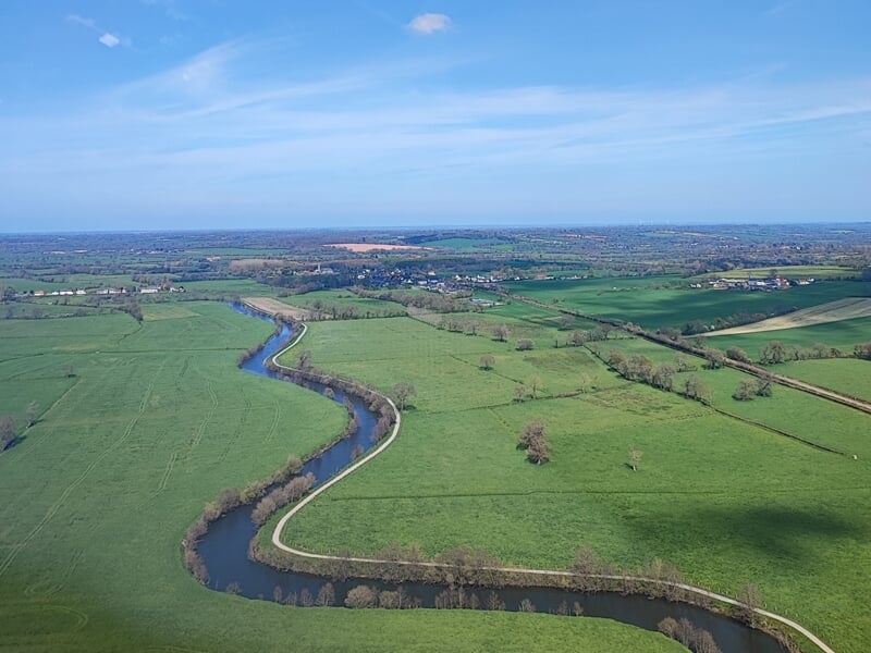 Image aérienne d'une rivière sinueuse traversant des prairies vertes lors d'un baptême en ulm autogire dans le Cotentin.