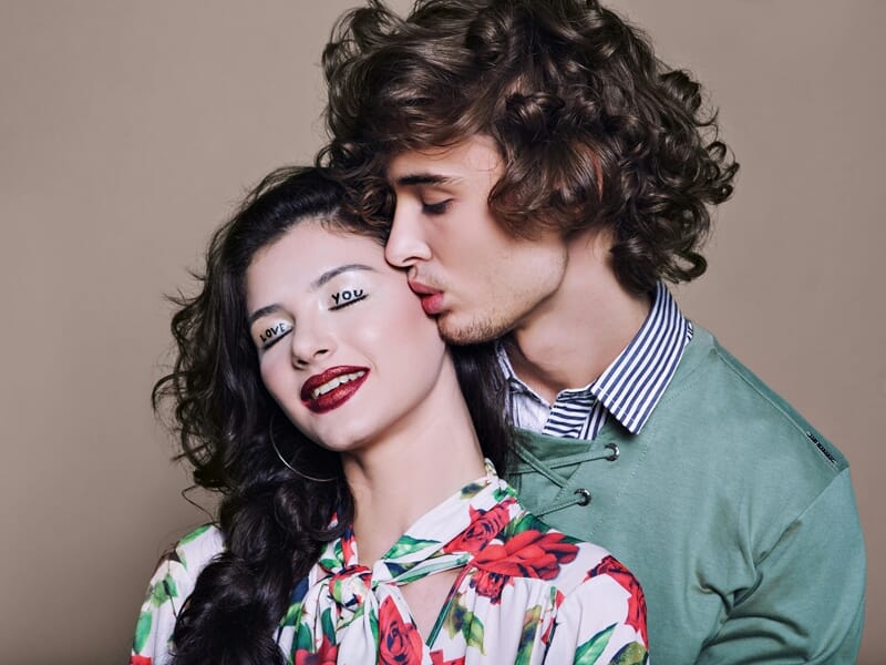 Un jeune homme aux cheveux bouclés embrasse tendrement une femme souriante lors d'un shooting photo couple près de Nancy.