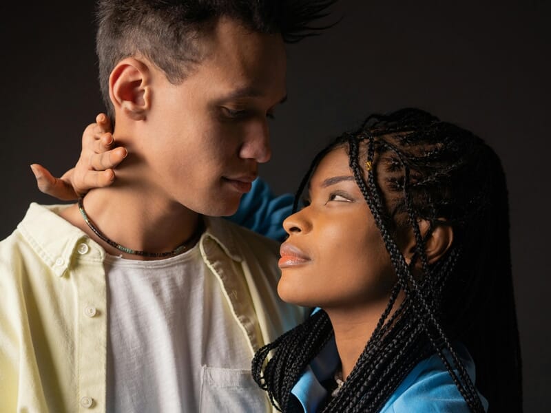Un couple se regarde intensément, la femme aux tresses noires touche doucement le cou lors d'un shooting photo couple près de Nancy.