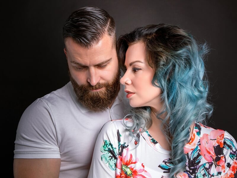Un homme barbu et une femme aux cheveux bleus se regardent avec douceur lors d'un shooting photo couple près de Nancy.