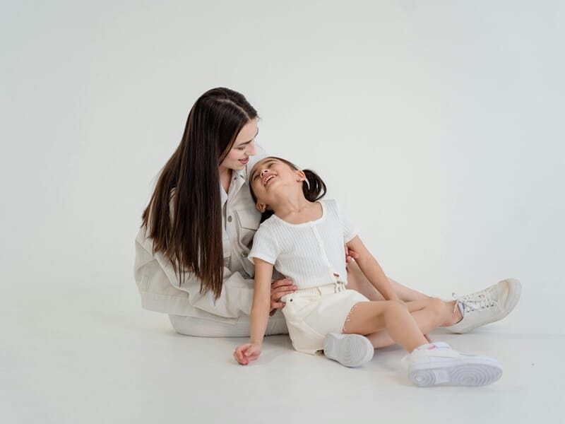 Une femme souriante assise par terre avec une petite fille riant lors d'un shooting photo de famille près de Nancy.