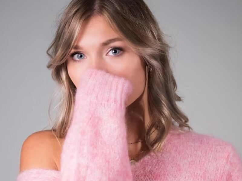 Portrait d'une femme blonde en pull rose doux, main devant la bouche, lors d'un shooting photo portrait près de Nancy.
