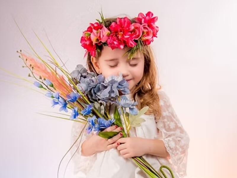 Petite fille en robe blanche avec couronne de fleurs, tenant un bouquet coloré lors d'un shooting photo portrait près de Nancy.