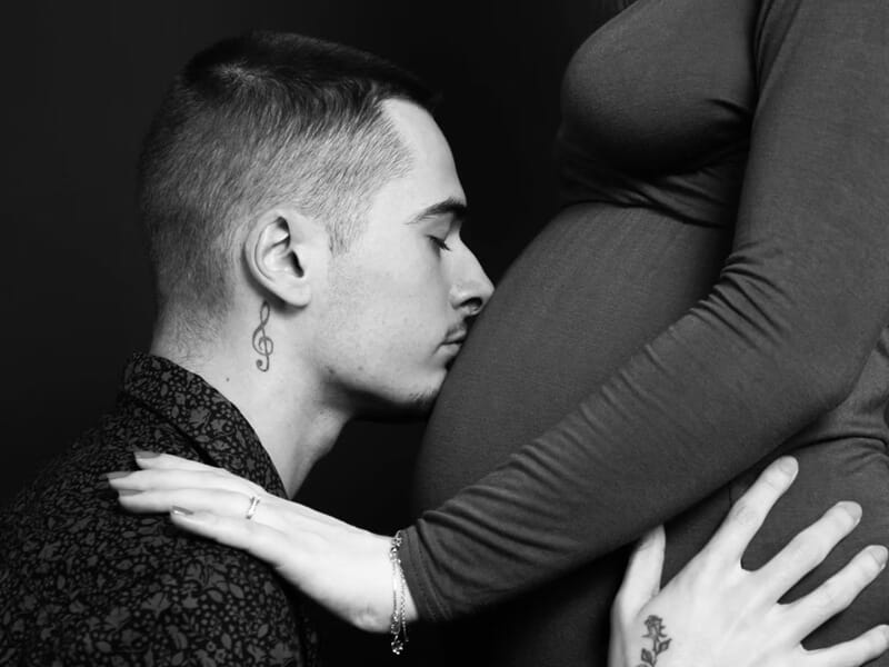 Homme embrassant tendrement le ventre d'une femme enceinte habillée en noir lors d'un shooting photo grossesse près de Nancy.
